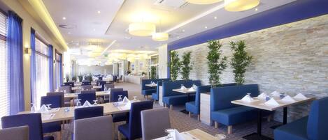 Un restaurante moderno con asientos de tapicería azul y mesas, pared de piedra y lámparas colgantes.