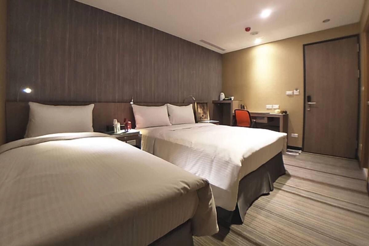 A hotel room with two beds, a desk, and a chair.
