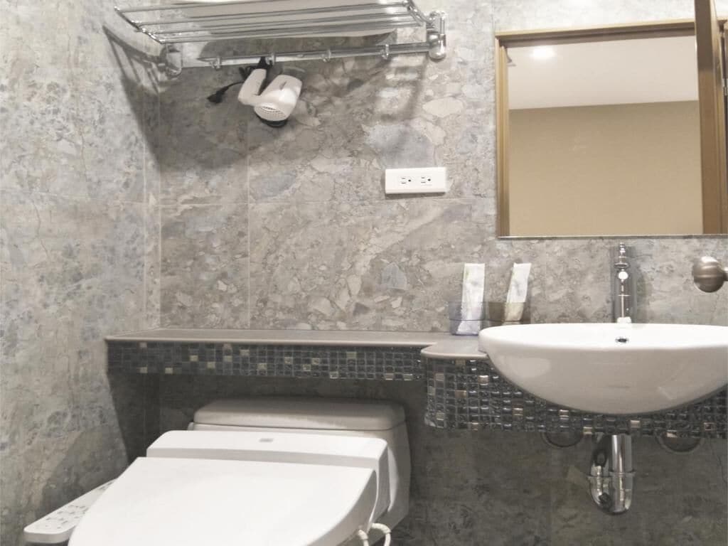 Un baño con pared de mármol, un lavabo blanco, un inodoro y un perchero para toallas.