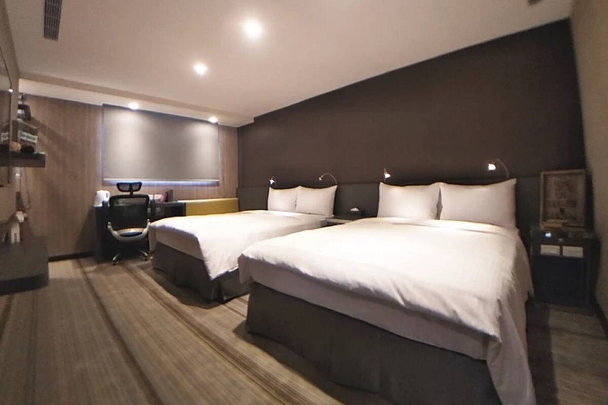 A hotel room with two beds, a desk, and a chair.