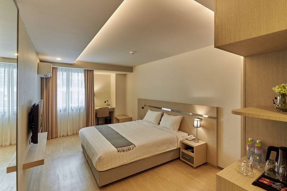 A modern hotel room with a large bed, bedside tables, a desk, and a wardrobe.