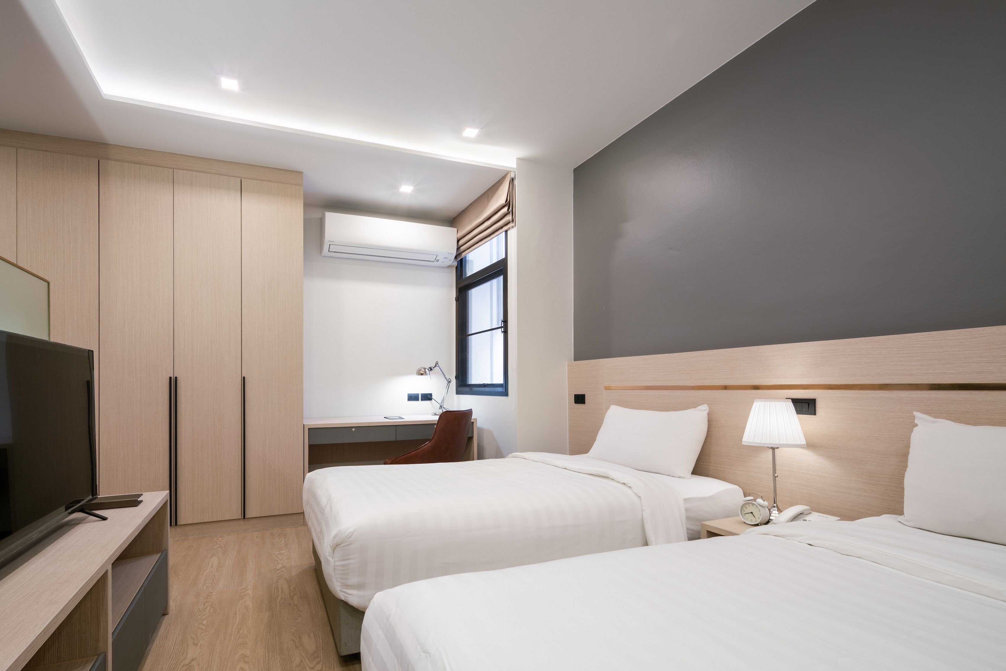 A hotel room with two beds, a TV, a desk, and a window with curtains.