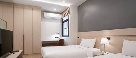 A hotel room with two beds, a TV, a desk, and a window with curtains.