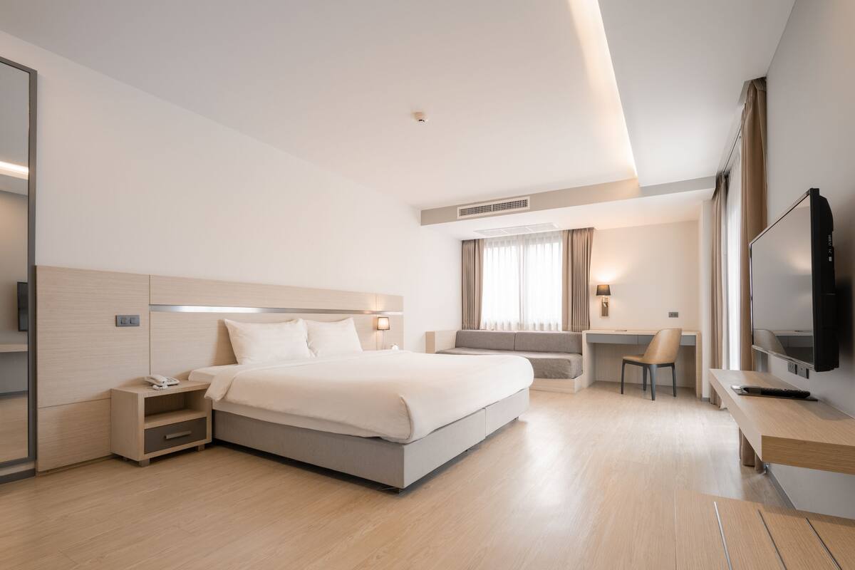 A modern hotel room with a large bed, a desk, a chair, a TV, and a bedside table with a phone.