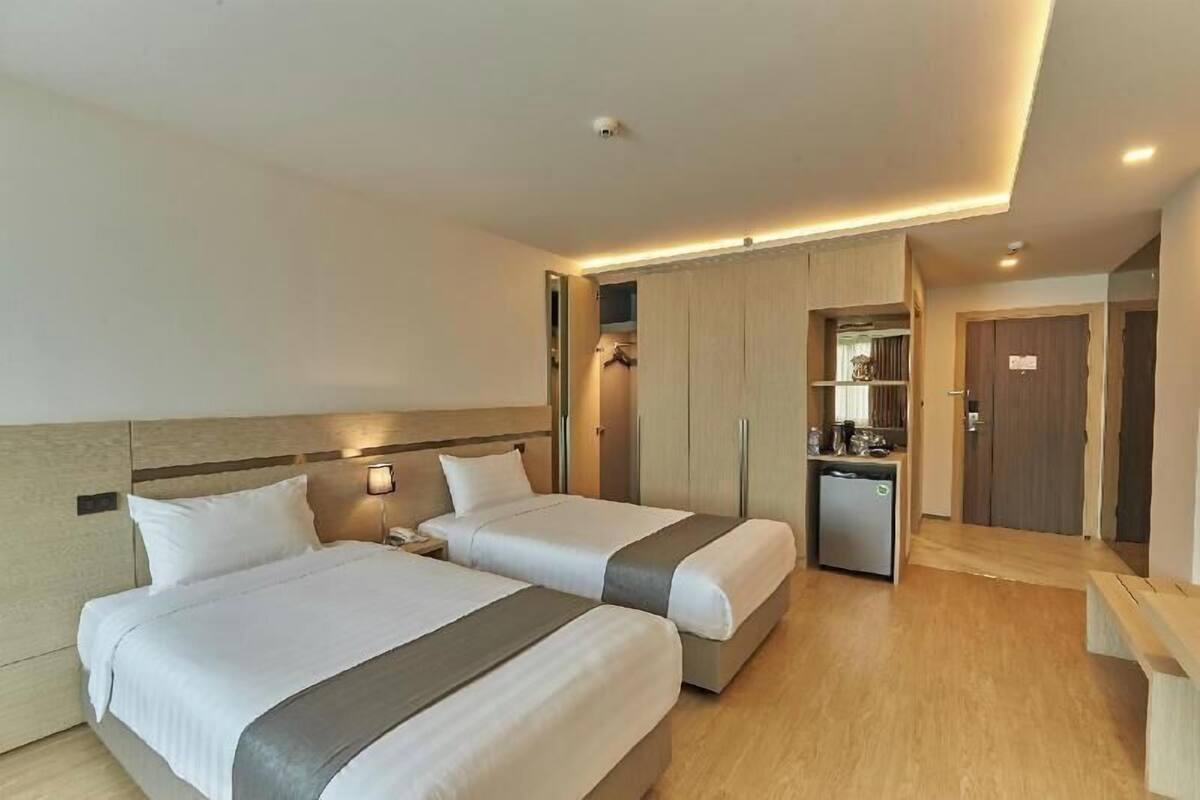 A hotel room with two beds, a small kitchenette, a wardrobe, and a bench.