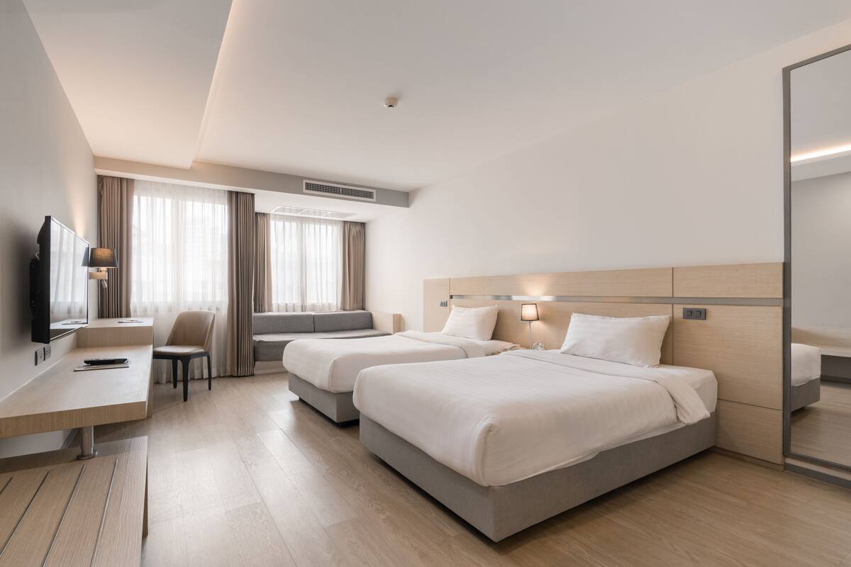 A modern hotel room with two beds, a desk, a chair, and a large mirror.
