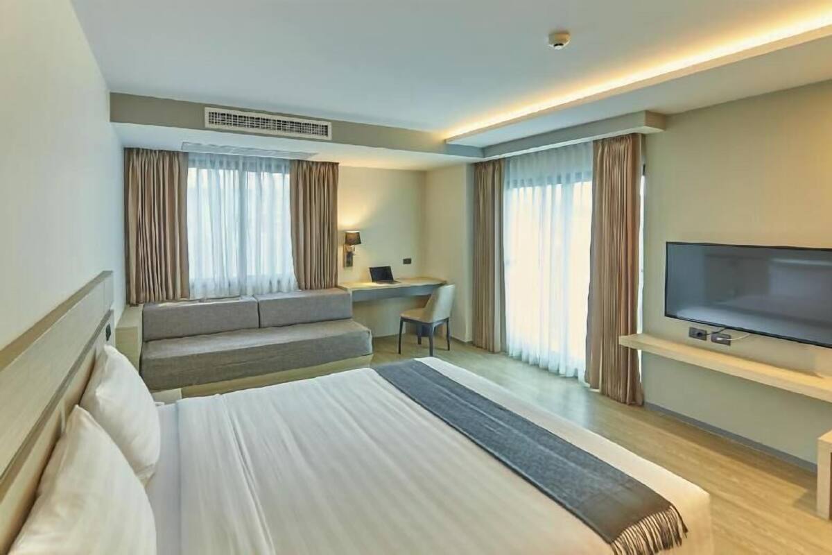 A hotel room with a large bed, a desk, a chair, a flat-screen TV, and a sofa.