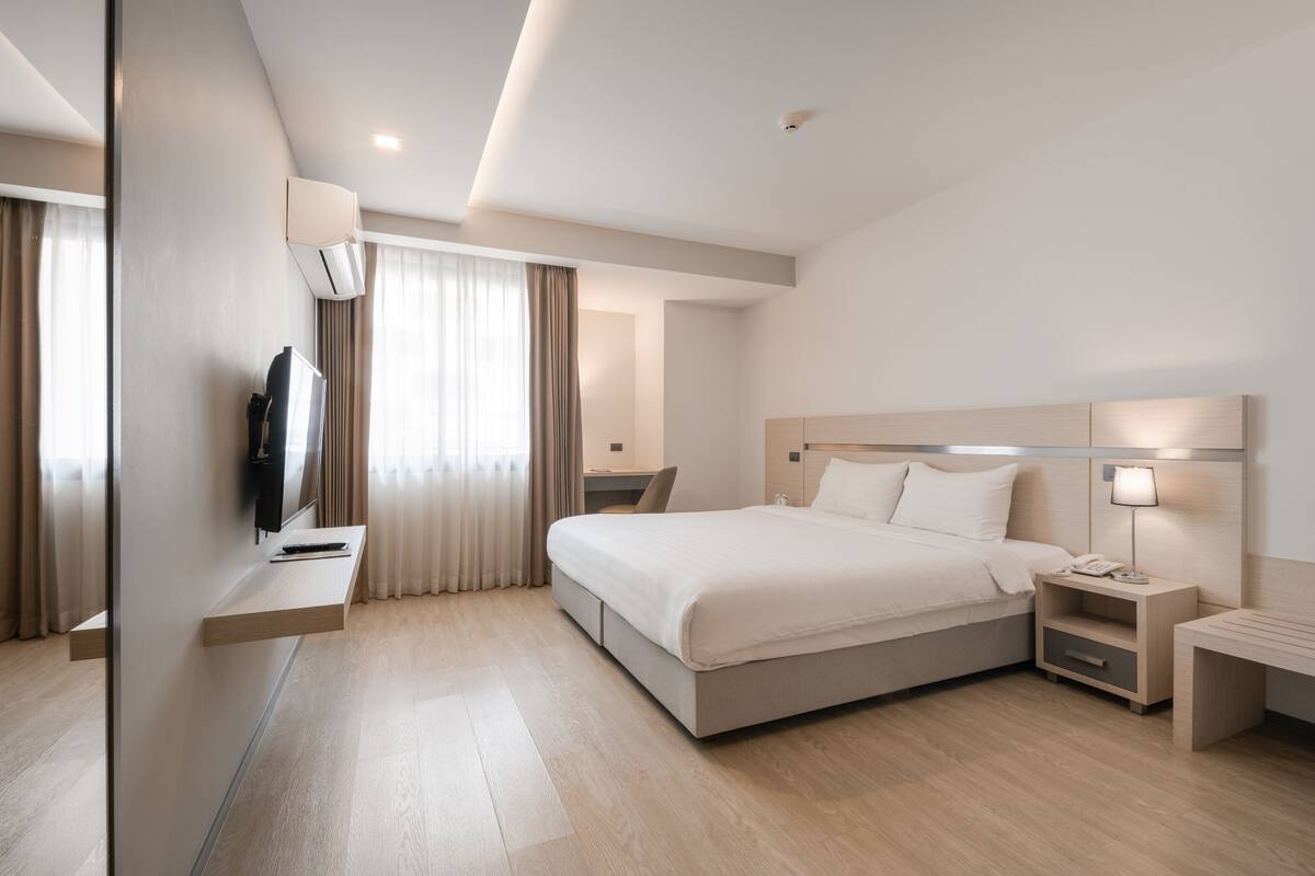 A modern hotel room with a large bed, bedside tables, a desk, and a television.