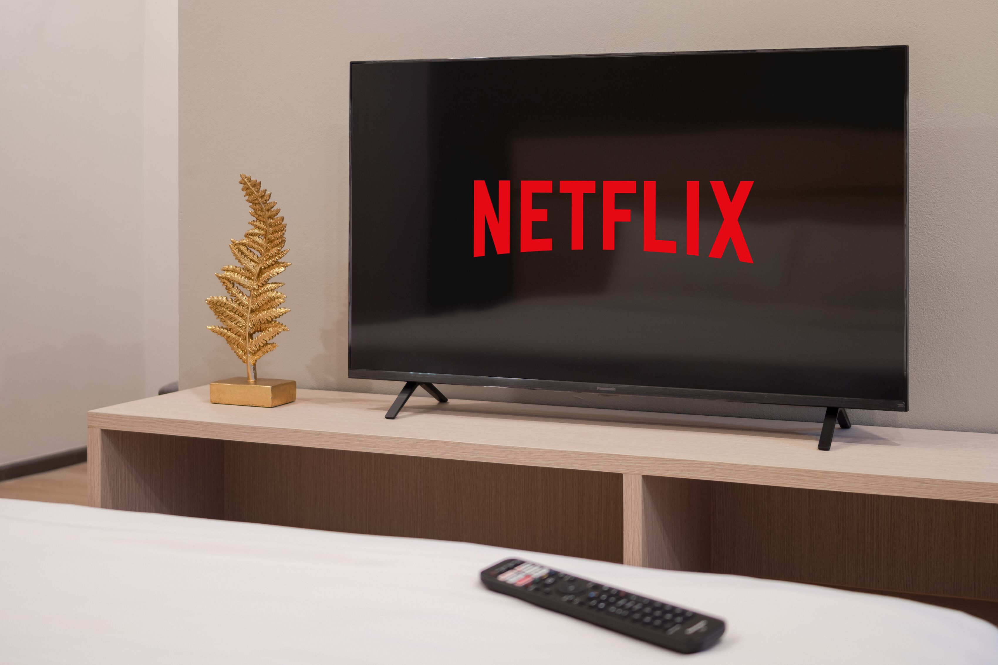 A television on a wooden stand with a remote control in front of it.