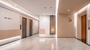 A modern hotel lobby with a clean, minimalist design, featuring a reception desk, a vertical light fixture, and a large number '6' on the wall. - Samyan Serene Hotel (Bangkok)