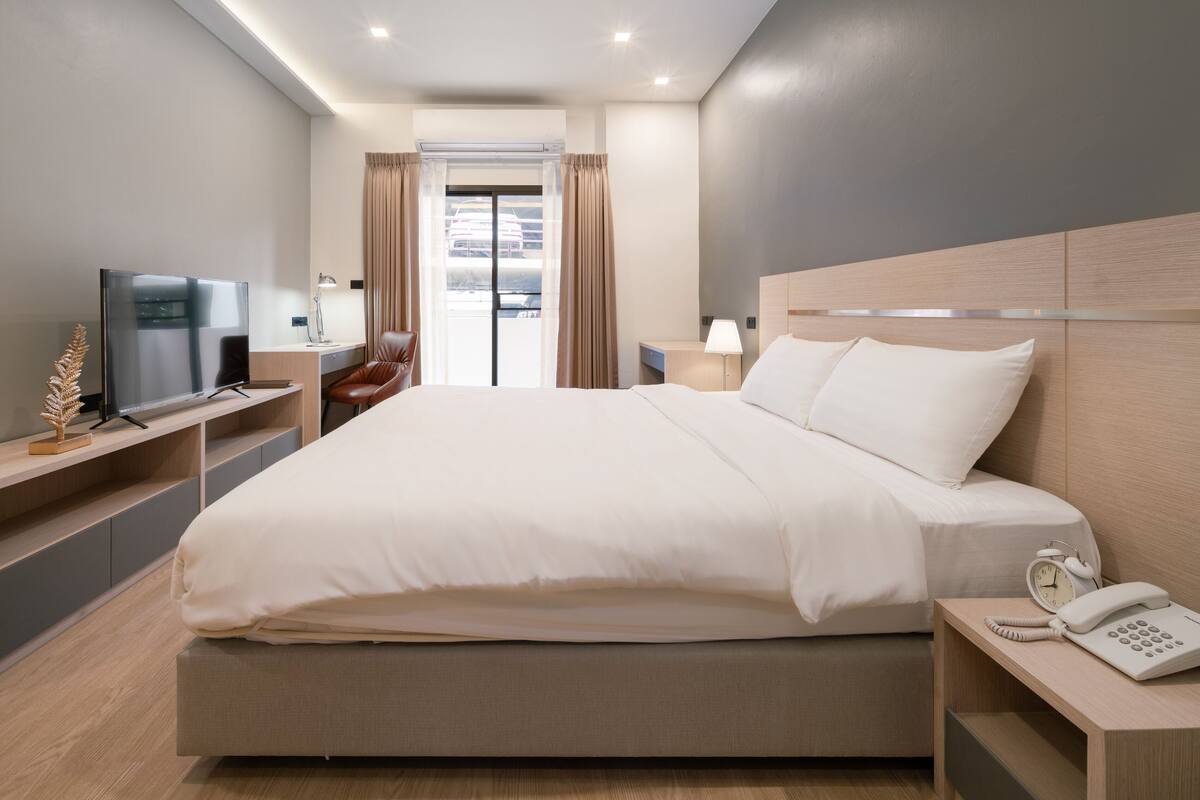 A modern hotel room with a large bed, bedside tables, a TV, and a view of the outside.