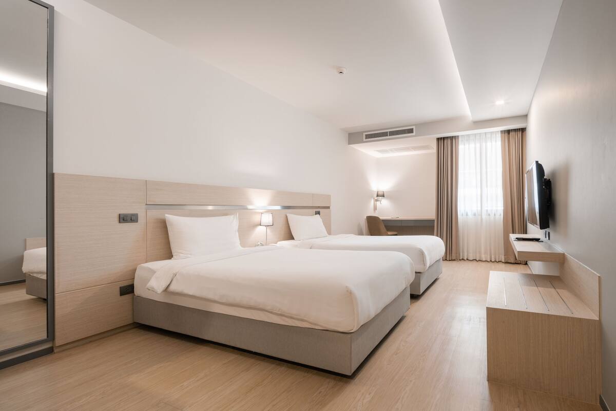 A modern hotel room with two beds, a desk, a TV, and a large mirror.
