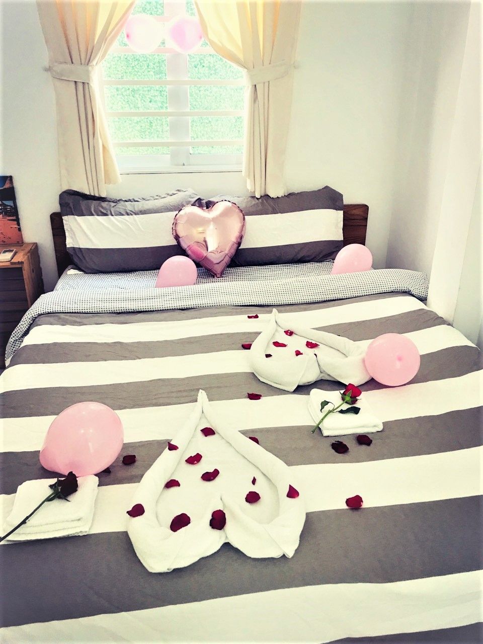 A bed with striped bedding, pillows, and a heart-shaped pillow.