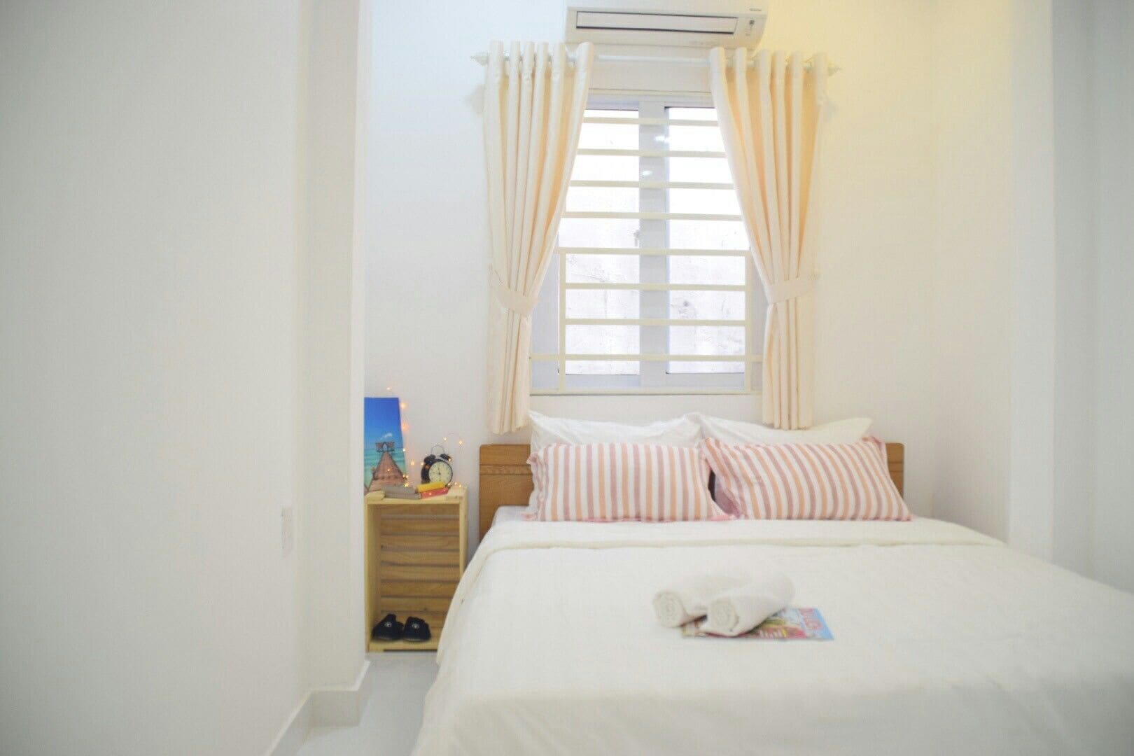 Un dormitorio con cama, mesita de noche, ventana con cortinas y un equipo de aire acondicionado.