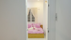 A narrow hallway leading to a bedroom with a bed, a window with curtains, and a door.