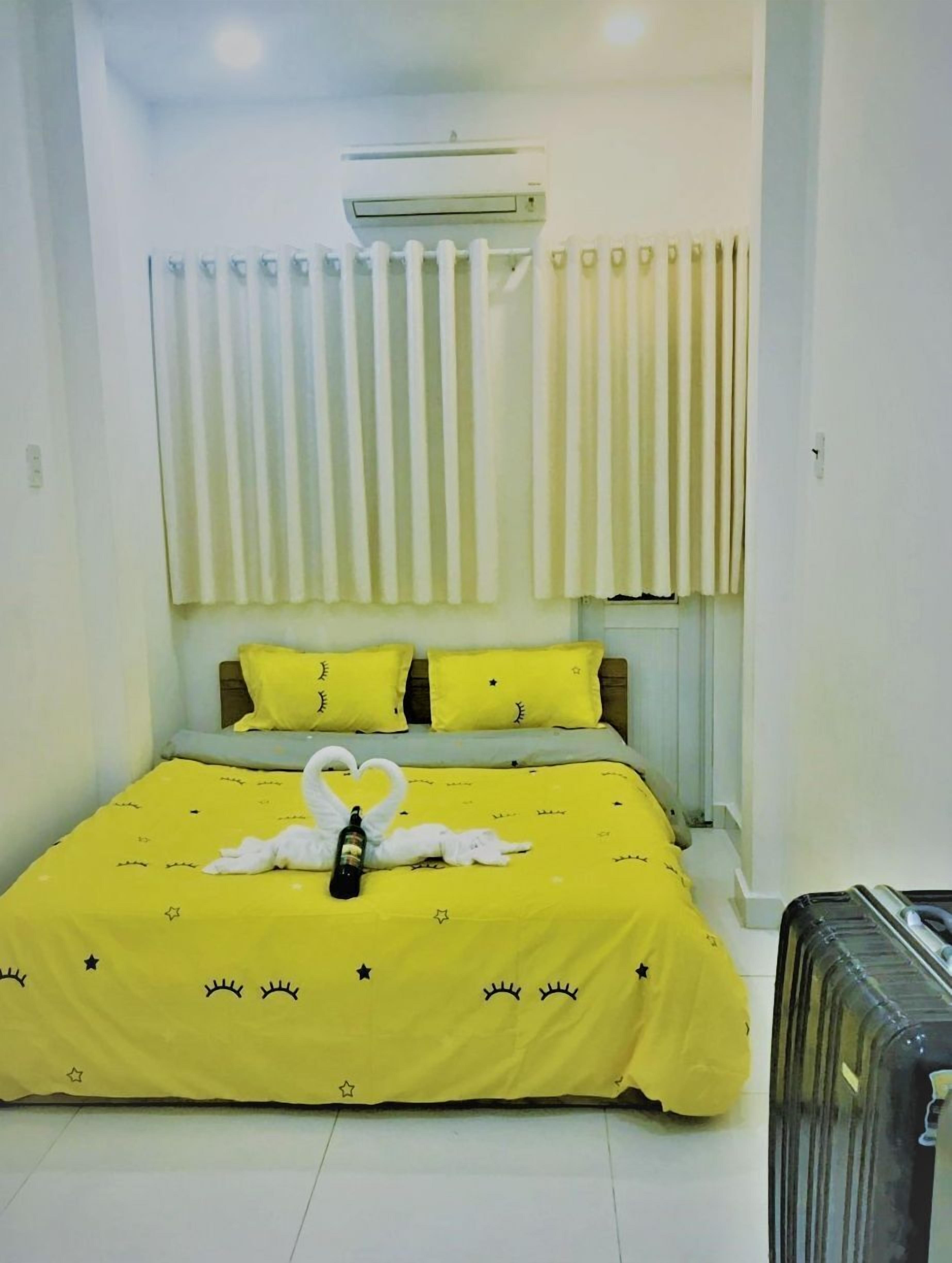 A hotel room with a bed, curtains, an air conditioning unit, and a suitcase.