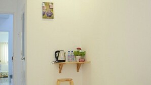 A hotel room with a bed, an air conditioner, a small shelf with toiletries, and a painting on the wall.