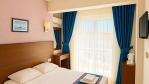 A hotel room with a large bed, a bedside table with a lamp, a TV, and a window with curtains. - Doruk Hotel and Suites (Marmaris)