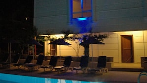 A swimming pool with lounge chairs and umbrellas, surrounded by a building with a tiled exterior. - Doruk Hotel and Suites (Marmaris)