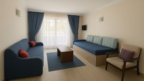 A modern living room with a sofa, a chair, a small table, and a bed with striped pillows. - Doruk Hotel and Suites (Marmaris)