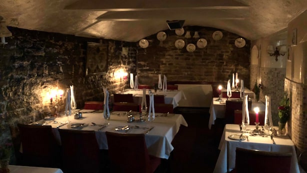 A dimly lit restaurant with stone walls and tables set for dining. - Candlesticks (Stamford)