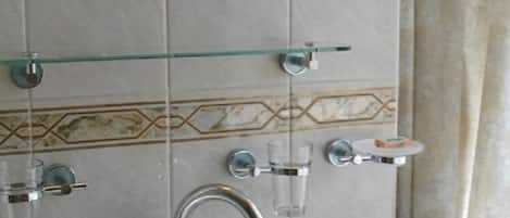 A bathroom with a white sink, a glass shelf with toiletries, a hairdryer, and a mirror.