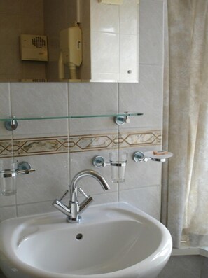 A bathroom with a white sink, a glass shelf with toiletries, a hairdryer, and a mirror.