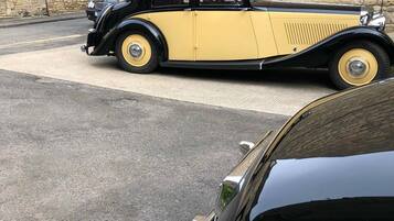 A vintage yellow and black car parked in front of a stone building with a sign indicating it is a car park for a hotel.