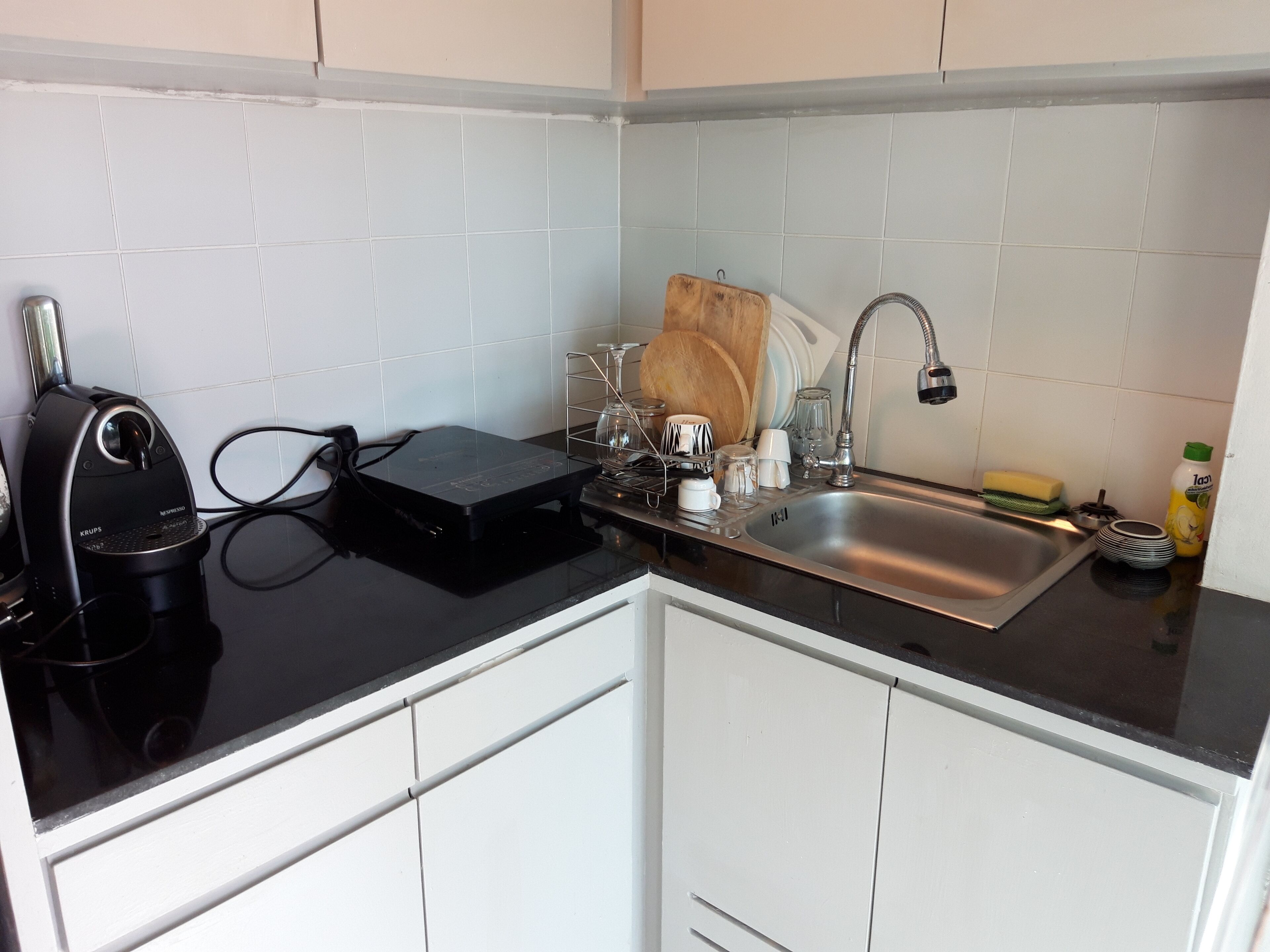 Cocina compacta con gabinetes blancos, encimera negra, pileta de acero inoxidable y cafetera Krups.