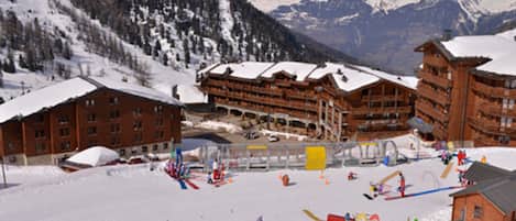 A ski resort with wooden buildings, a ski lift, and a snowy mountain backdrop.