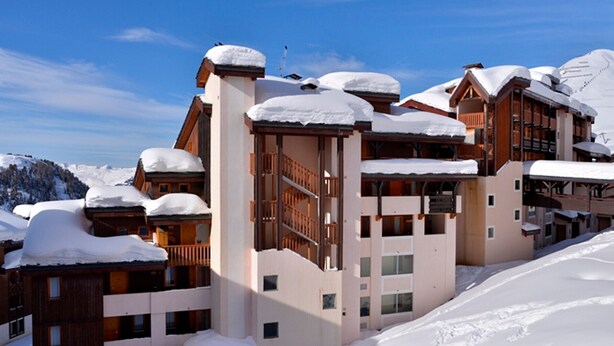 A snow-covered multi-story hotel with balconies and ski slopes in the background.