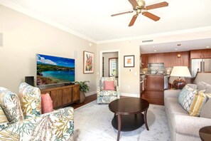 A living room with a flat-screen TV, a ceiling fan, a round coffee table, and a sofa.