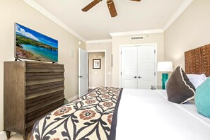 A bedroom with a bed, a dresser, a ceiling fan, and a painting of a landscape.