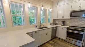A modern kitchen with white cabinets, a stainless steel oven, and a window with a view of trees. - Resort Home near Lake Michigan with Golf Cart (Michigan City)