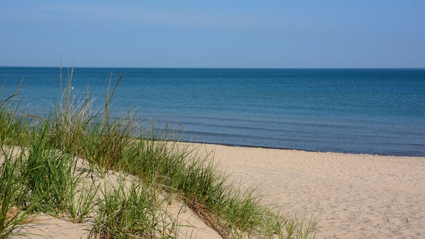 A beach with sand and grass in the foreground and a calm sea in the background. - Resort Home near Lake Michigan with Golf Cart (Michigan City)