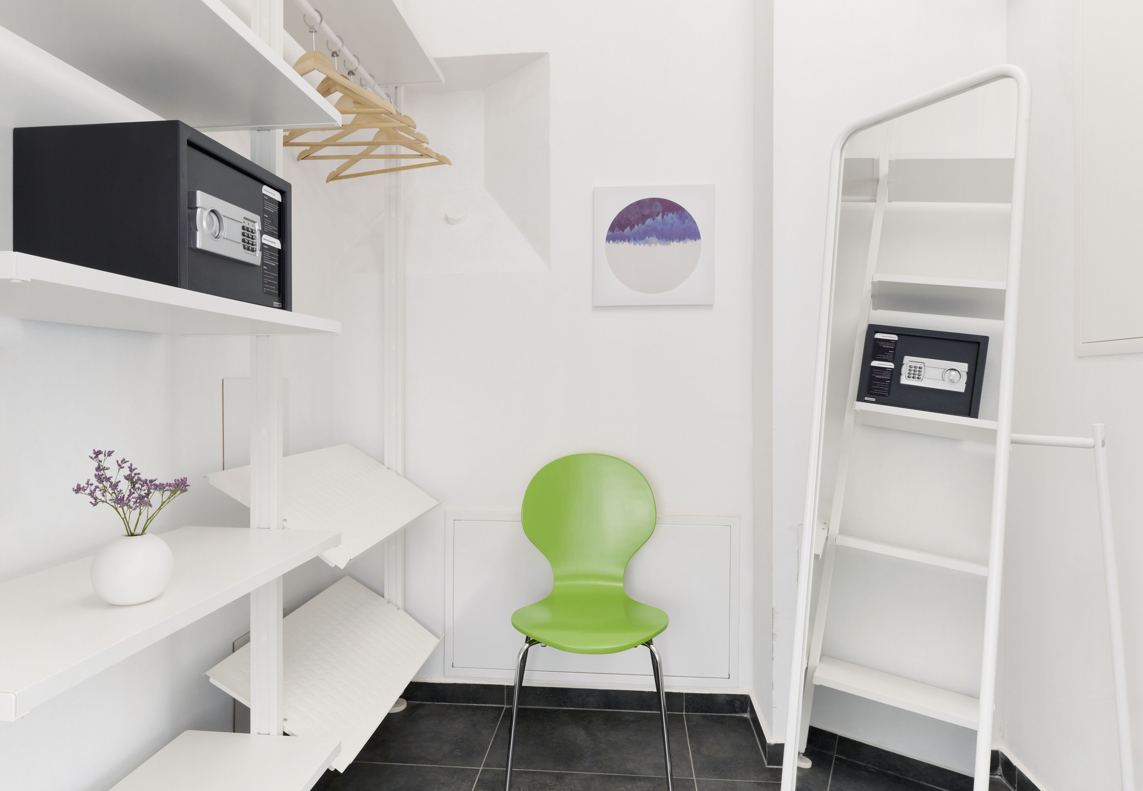 Un interior moderno y blanco con una silla verde, estanterías blancas y una caja fuerte negra.