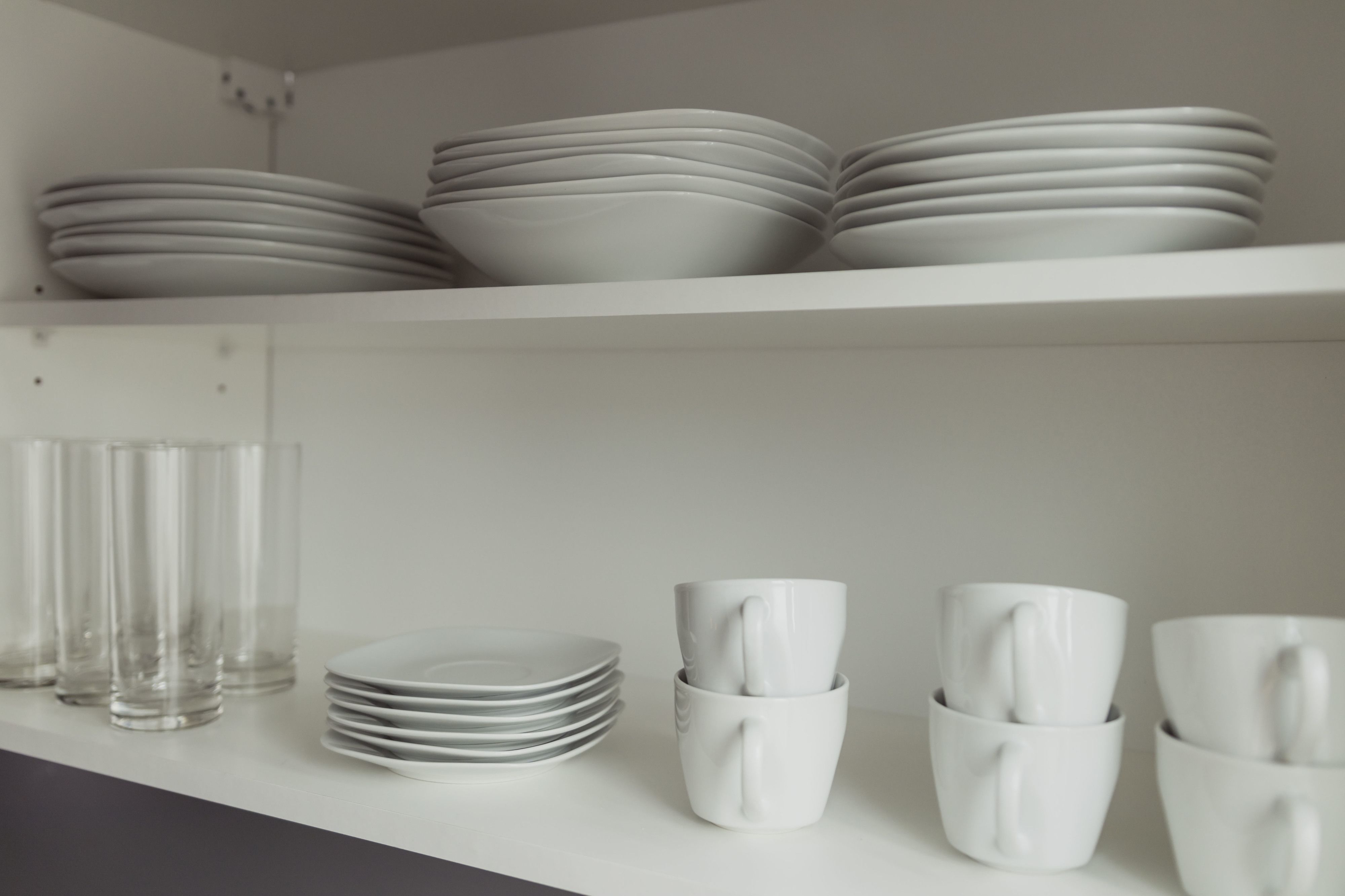 A kitchen with white plates, bowls, and cups stacked on shelves.