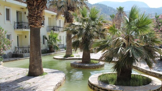 A courtyard with palm trees, a water feature, and a building with balconies. - Hierapolis Termal Hotel (Denizli)