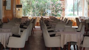 A dining area with tables and chairs, large windows with a view of greenery and flowers, and a wall-mounted air conditioning unit. - Hierapolis Termal Hotel (Denizli)
