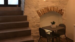 Ein gemütliches Zimmer mit Steinwand, Kamin, Esstisch mit Stühlen und einer Treppe, die zu einer oberen Ebene führt.