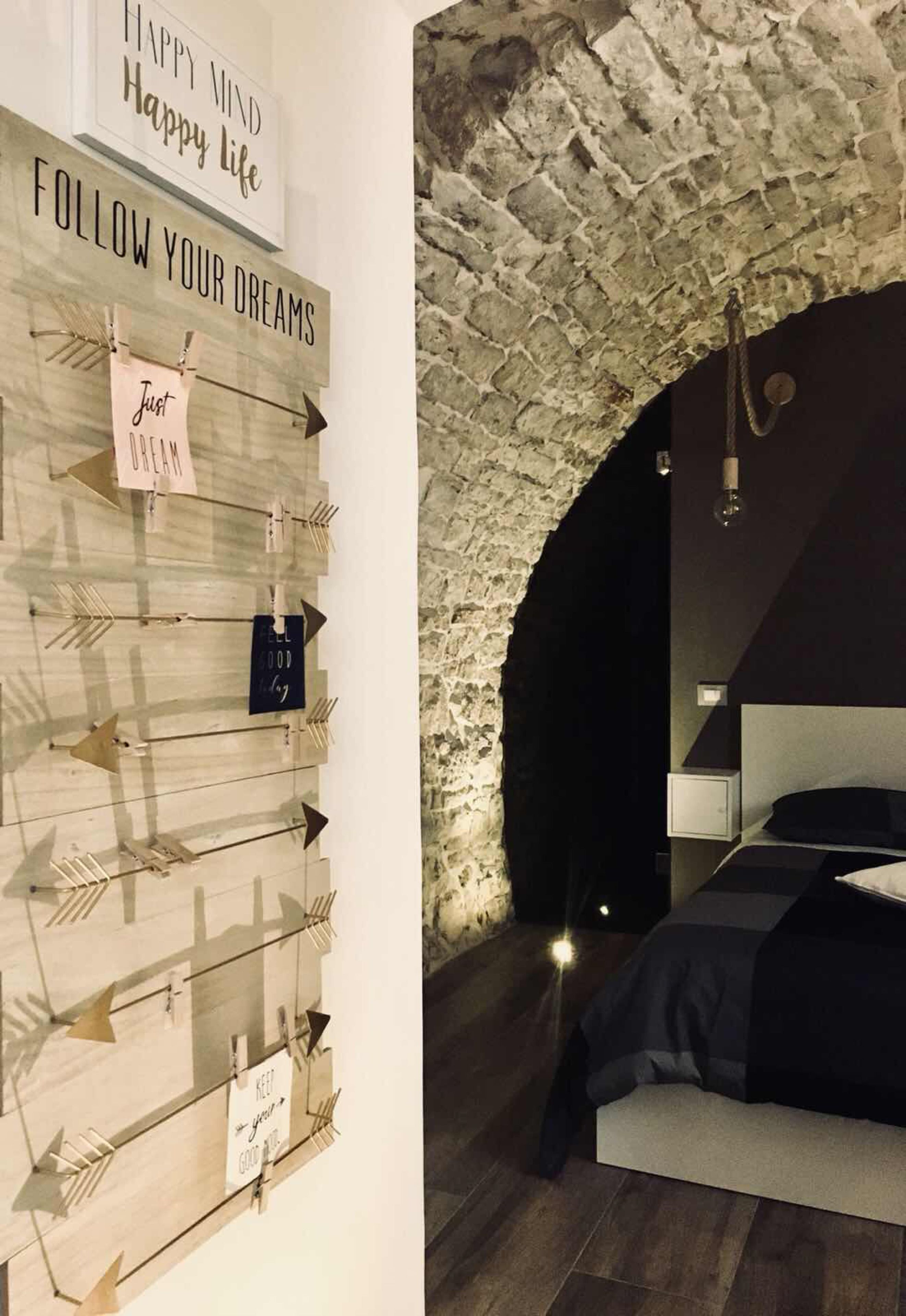 A bedroom with a stone archway, a wooden wall with motivational signs, and a bed with a dark-colored headboard.