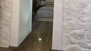 Ein Schlafzimmer mit Steinwand, Holzboden und einem Bett mit gestreifter Bettdecke.