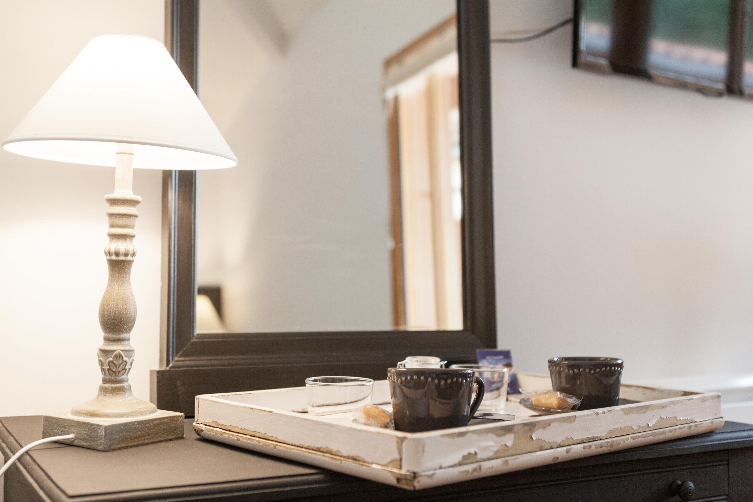 A bedside table with a lamp, a tray with a cup, a small bowl, and a decorative item.