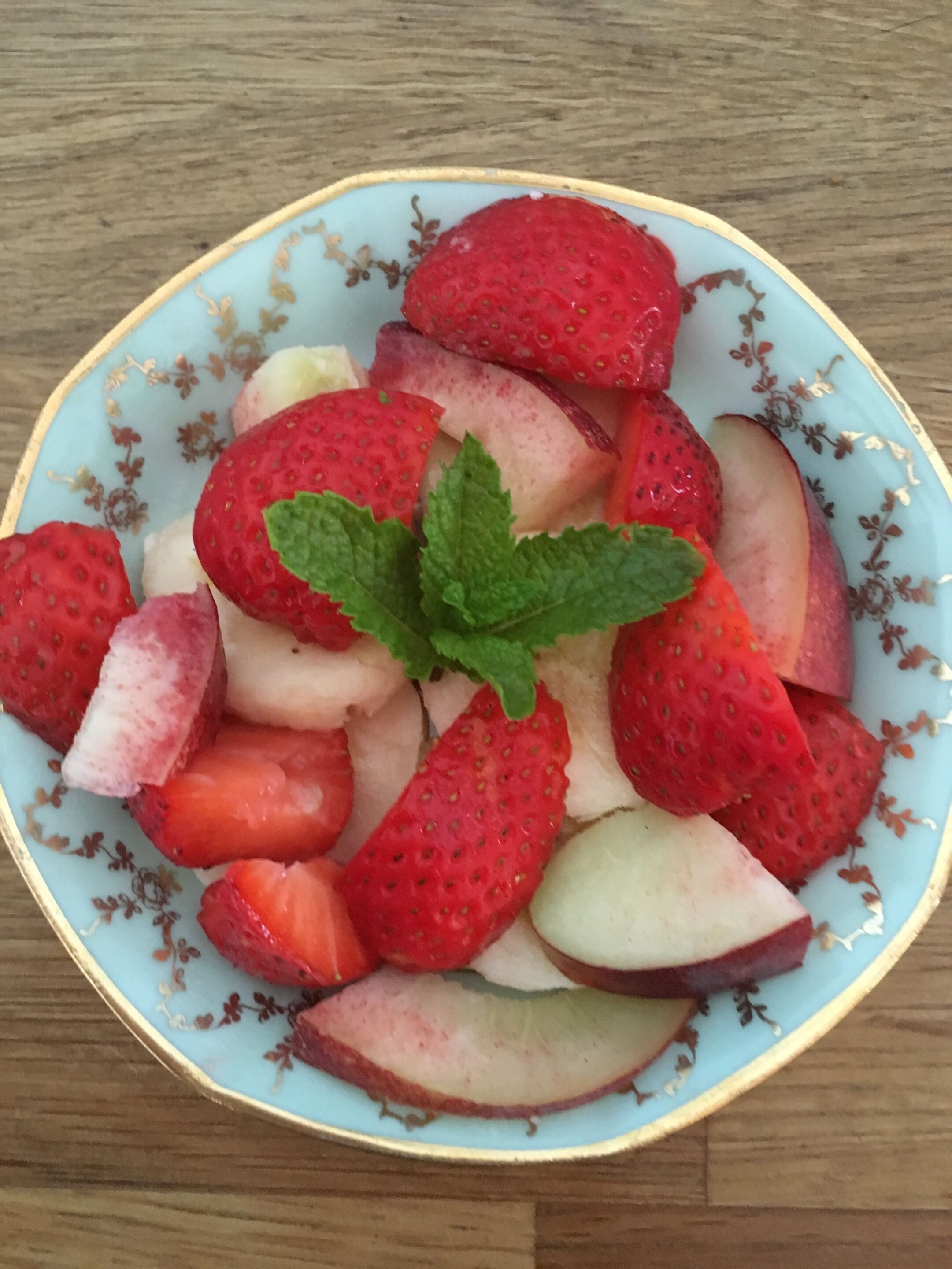 Un bol de fraises et de pommes coupées en tranches, disposées sur une assiette à motifs floraux.