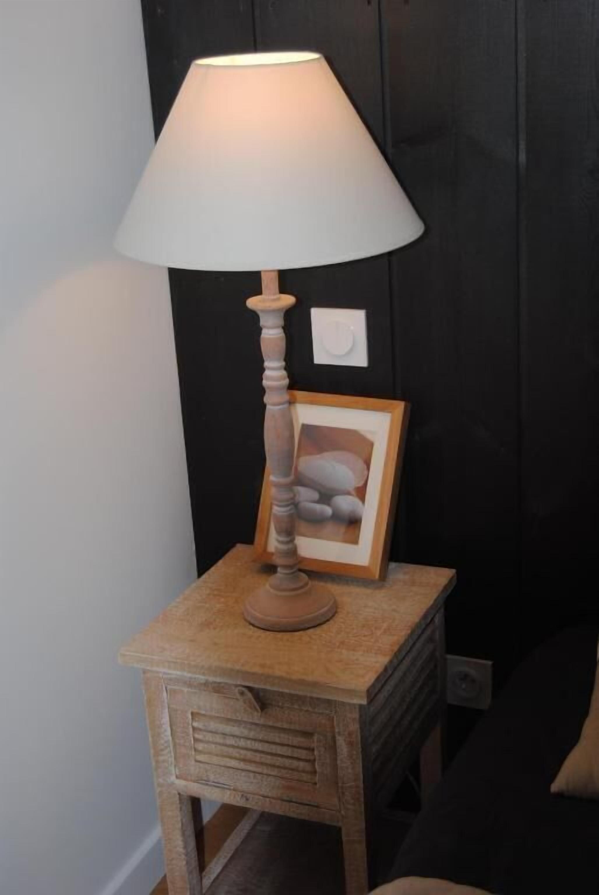 Una mesita de noche de madera con una lámpara y un cuadro enmarcado.