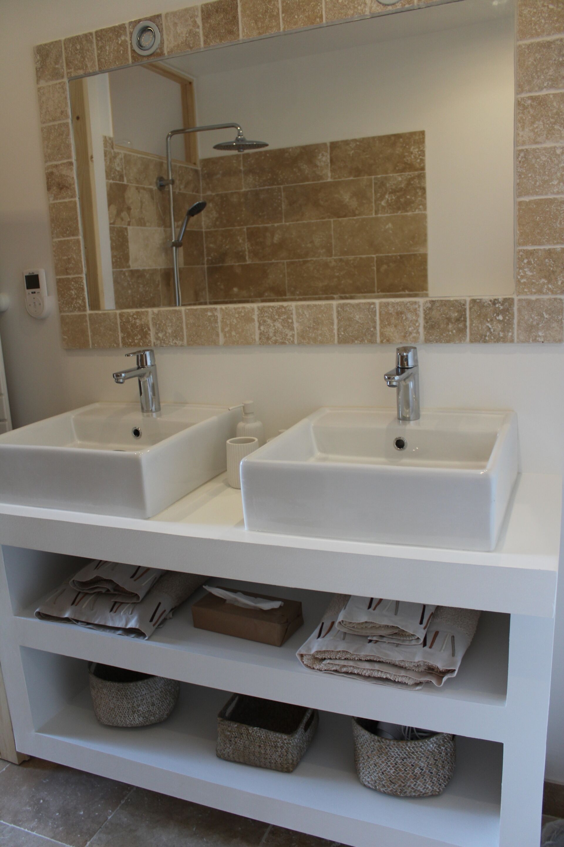 A bathroom with two sinks, a mirror, and storage shelves with folded towels and baskets.