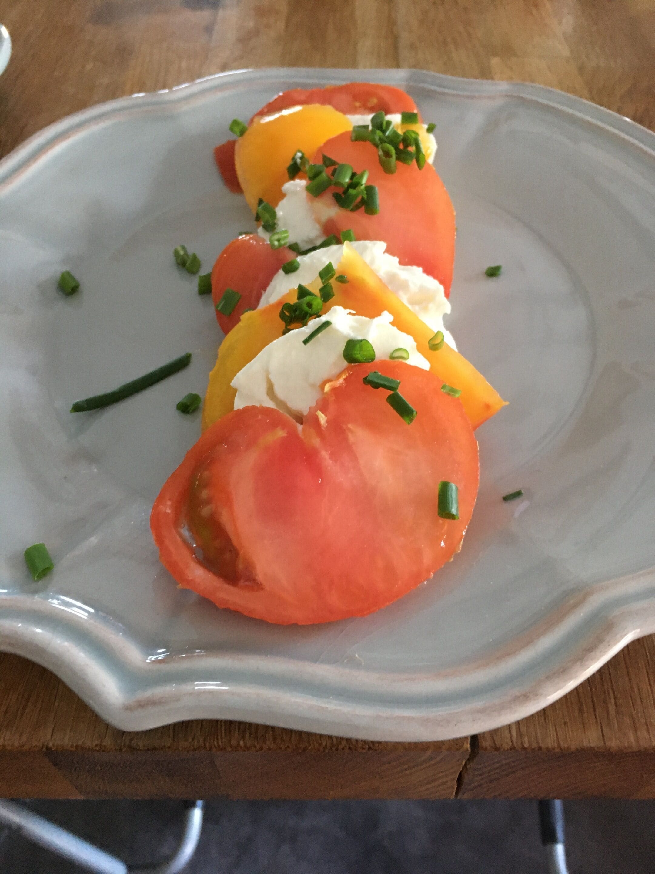A plate of sliced tomatoes, yellow squash, and cream cheese garnished with chives.