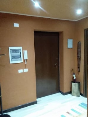 A room with a brown door, a wall-mounted electrical panel, and a small trash bin. - B&B Al Calopinace (Reggio Calabria)