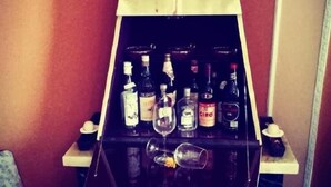 Una zona de bar con un estante de vidrio que contiene varias botellas y copas.