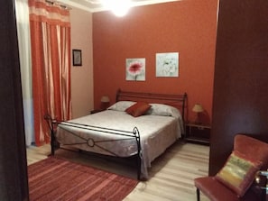 A bedroom with a bed, two bedside tables, a chair, a red curtain, and two wall-mounted pictures. - B&B Al Calopinace (Reggio Calabria)